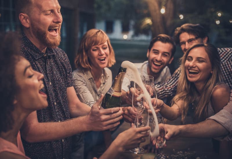 Young man splashing while opening champagne on a night party with his friend.