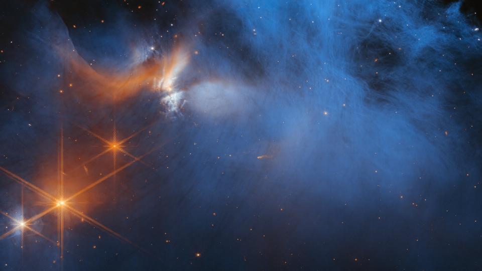 A wispy blue cloud of molecular gas glows from the light of distant stars in this James Webb Space Telescope image