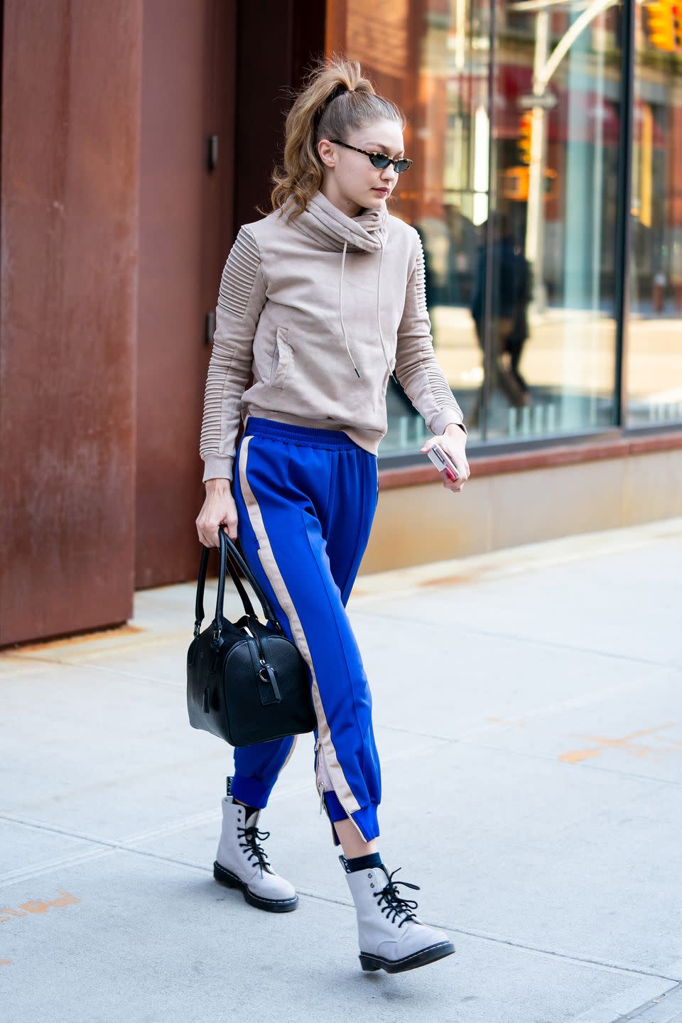 <p>In a khaki hoodie, blue sweat pants with white stripes down the side, white combat boots, tiny sunglasses, and a black handbag.</p>