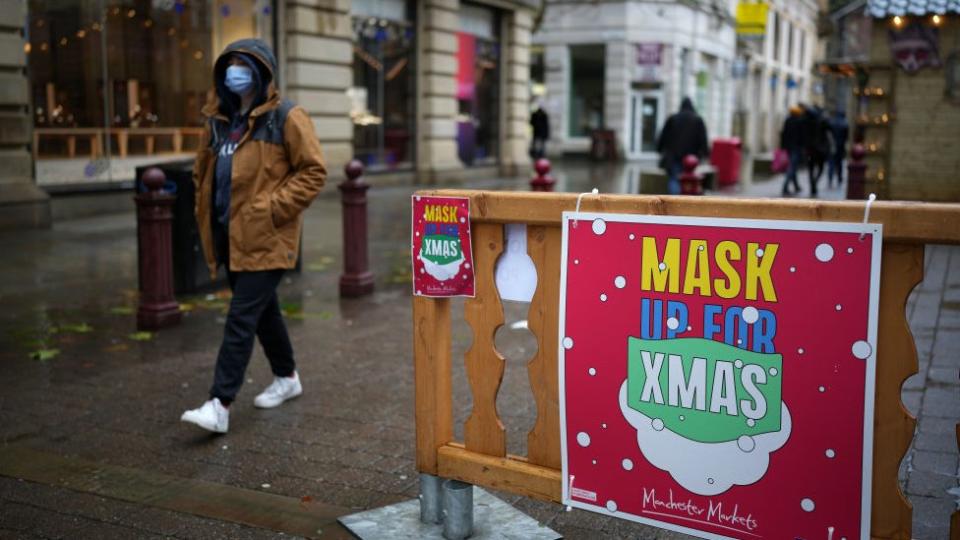 Foto de una persona caminando cerca de un letroro que pide usar mascarillas contra la covid'19