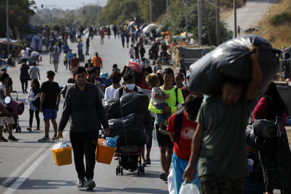 Migrants carry their belongings as they flee a road leading from Moria to the capital of Mytilene, on the northeastern island of Lesbos, Greece, Thursday, Sept. 17, 2020. A Greek police operation is underway on the island of Lesbos to move thousands of migrants and refugees left homeless after a fire destroyed their overcrowded camp, into a new facility on the island. (AP Photo/Petros Giannakouris)