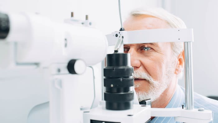 A bearded man's eyes being examined by optometrist or ophthalmologist using a phoropter.