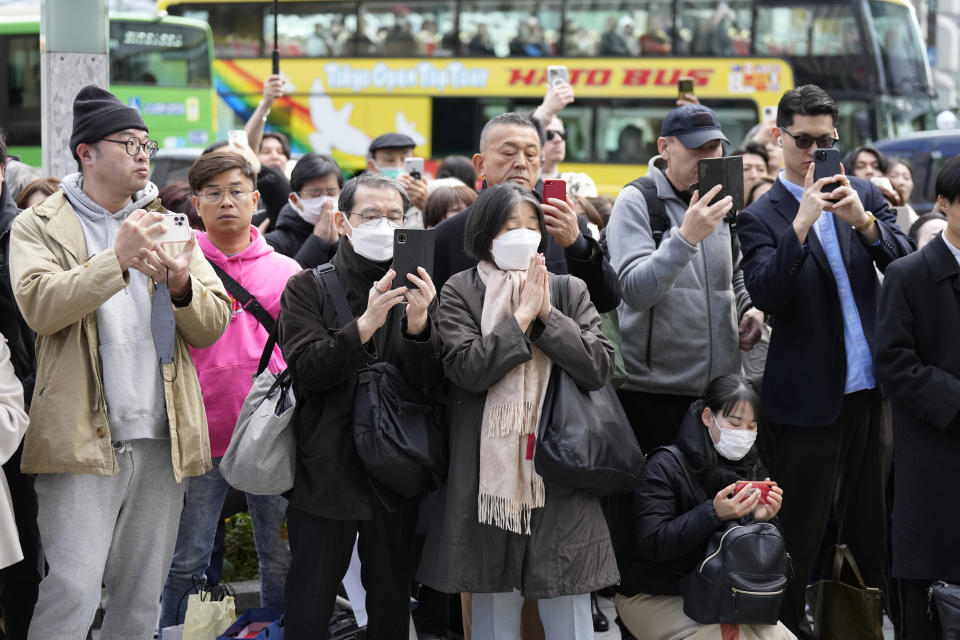 People hold phone as some pray when an annual tribute started at 2:46 p.m. for the victims of a 2011 disaster Monday, March 11, 2024, in Tokyo. Japan on Monday marked the 13th anniversary of the massive earthquake, tsunami and nuclear disaster that struck Japan's northeastern coast. (AP Photo/Eugene Hoshiko)