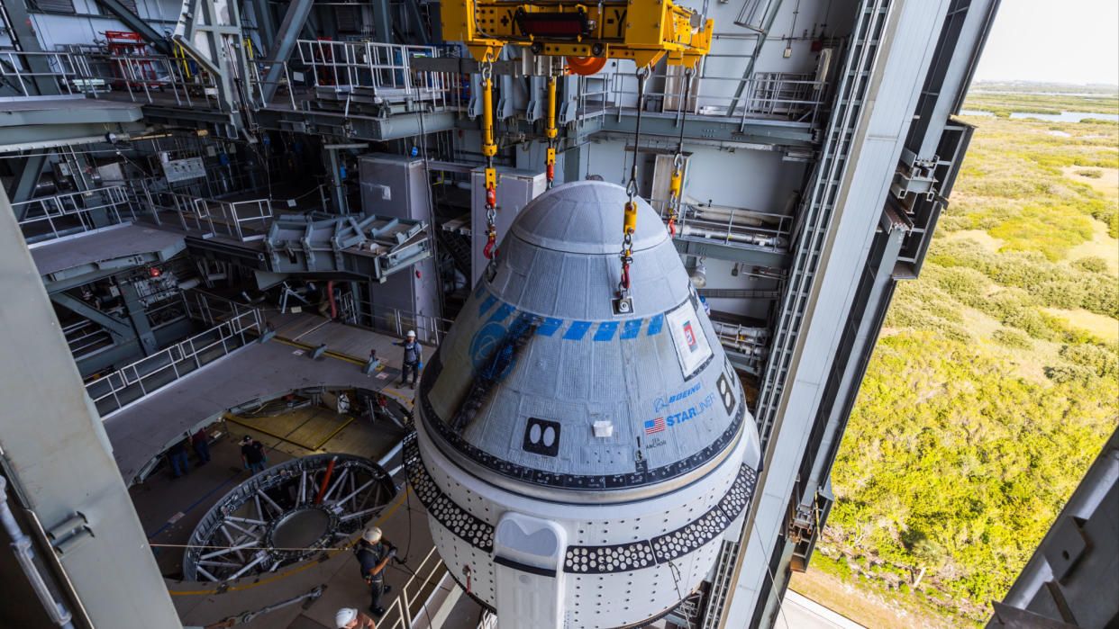  A cone-shaped spacecraft inside a tall facility with an open door to the right, showing trees and swamp down below. 