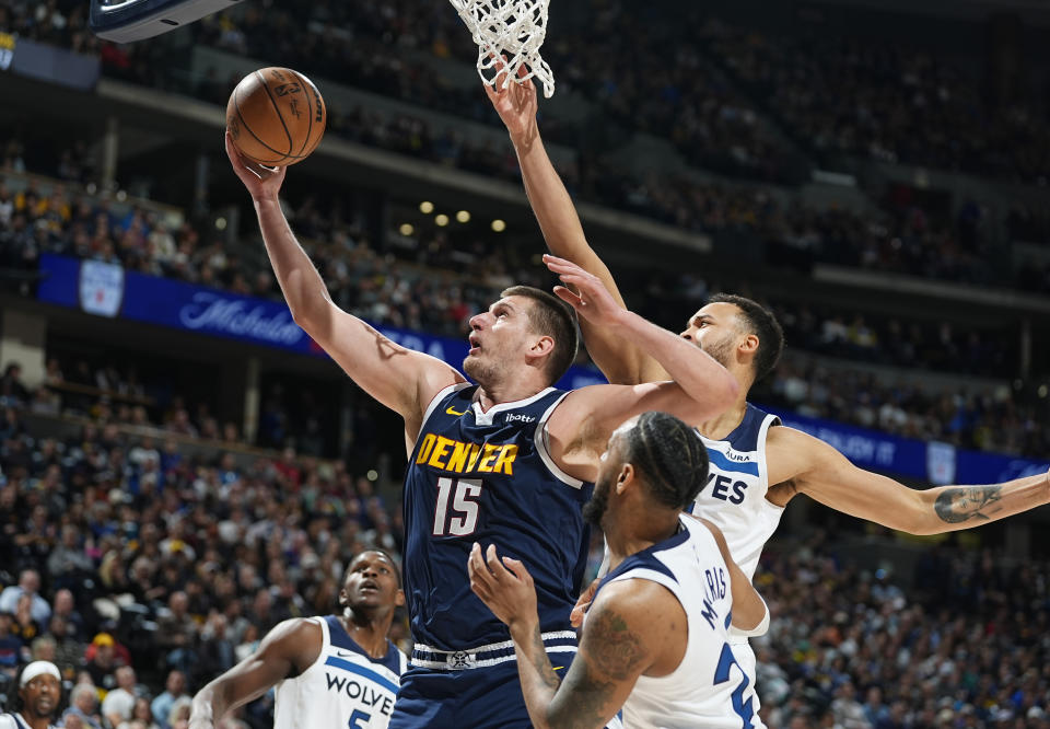 Denver Nuggets center Nikola Jokic (15) shoots goes as Minnesota Timberwolves guard Monte Morris, front right, and forward Kyle Anderson defend during the first half of an NBA basketball game Wednesday, April 10, 2024, in Denver. (AP Photo/David Zalubowski)