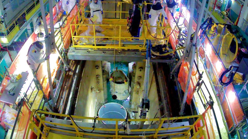 Teams use a 20-ton overhead crane to move the lower reactor vessel of the Oak Ridge Research Reactor into a cask for eventual shipment and disposal.