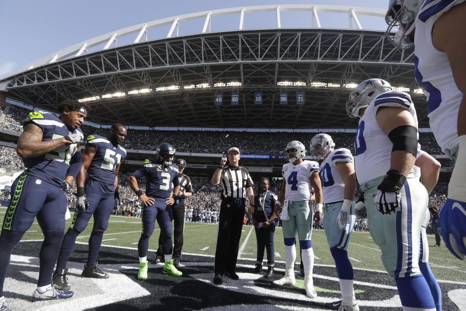 Referee Carl Cheffers, center, flips the coin as Seattle Seahawks quarterback Russell Wilson (3), Dallas Cowboys quarterback Dak Prescott (4), and other team captains look on before an NFL football game, Sunday, Sept. 23, 2018, in Seattle. (AP Photo/Elaine Thompson)