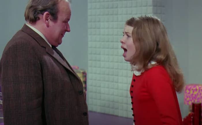 Veruca Salt, wearing a red dress, is yelling at a man in a tweed suit in a scene from "Willy Wonka & the Chocolate Factory."