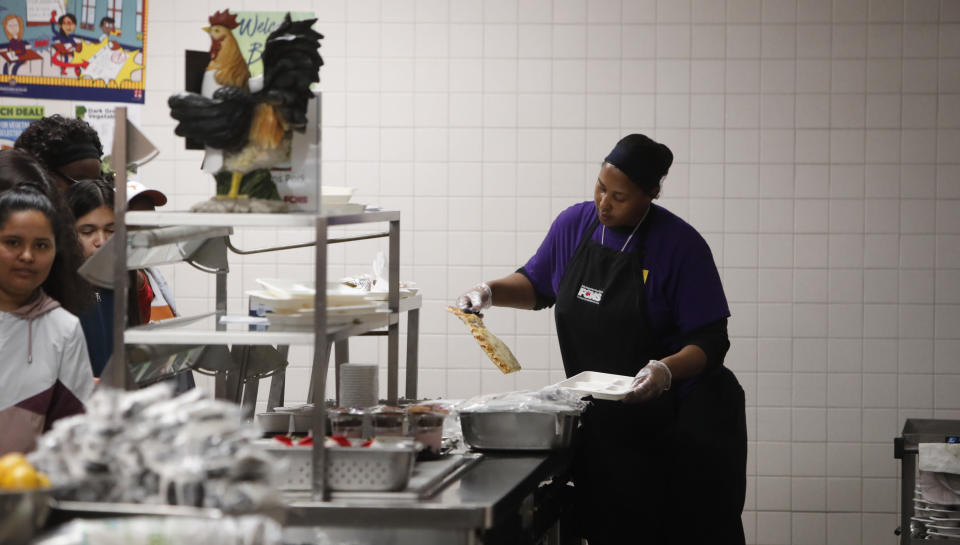 Nicole Johnson prepares lunch for students lined up in the cafeteria at Lincoln High School in Dallas, Friday, March 13, 2020. During the coming extended spring break school closures, this cafeteria and a few others in the Dallas Independent School District will be providing lunches to students despite the closure of the school. (AP Photo/LM Otero)