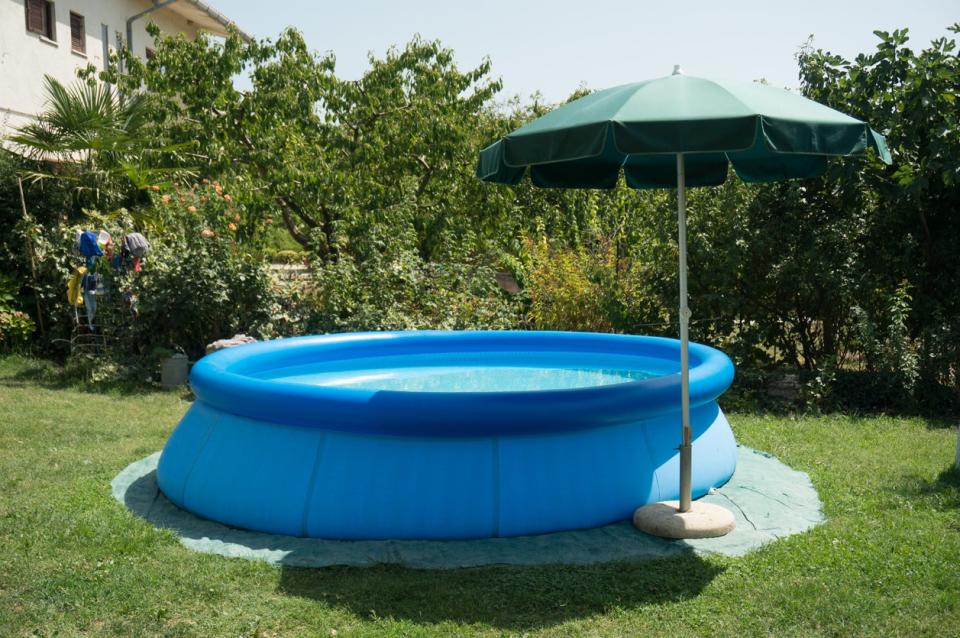 Inflatable above ground pool shaded by a green umbrella in a backyard