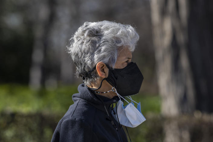 A woman wearing multiple face masks walks in the Retiro park in Madrid, Spain, Wednesday, Jan. 12, 2022. Italy, Spain and other European countries are re-instating or stiffening mask mandates as their hospitals struggle with mounting numbers of COVID-19 patients. (AP Photo/Bernat Armangue)