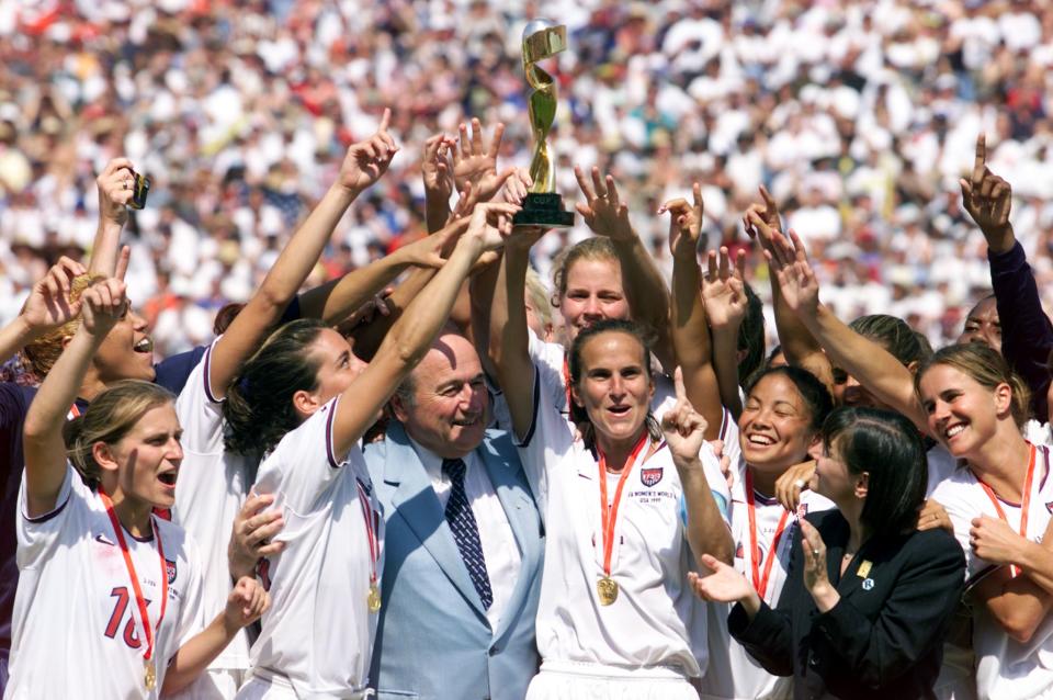 Carla Overbeck (C) holds up the World Cup trophy along with the rest of the US team after beating China to win the 1999 Women's World Cup 10 July 1999 at the Rose Bowl in Pasadena. With her is FIFA President Sepp Blatter. (ELECTRONIC IMAGE) AFP PHOTO/Hector MATA (Photo by HECTOR MATA / AFP) (Photo credit should read HECTOR MATA/AFP via Getty Images)