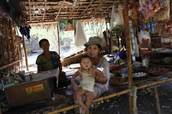 People sit in a shop below posters of Myanmar pro-democracy leader Aung San Suu Kyi and her father General Aung San in Phwartheinkha village in Kawhmu township, February 8, 2012.