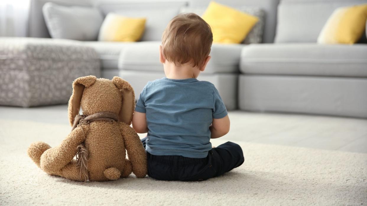 Un niño pequeño sentado de espaldas junto a su oso de peluche