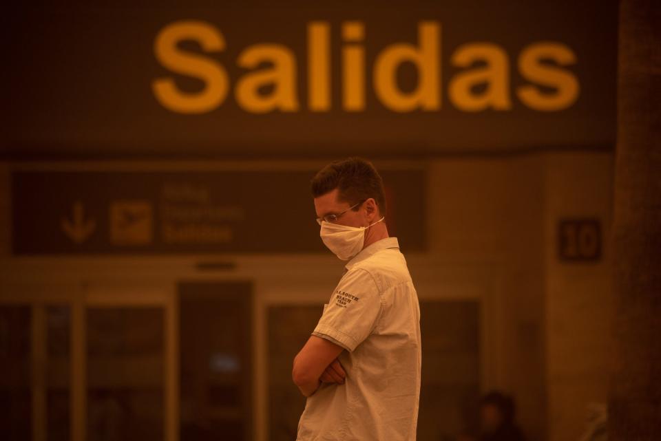 A man wearing a mask stands outside Tenerife SouthReina Sofia Airport during a sandstorm on February 23, 2020 on the Canary Island of Tenerife.