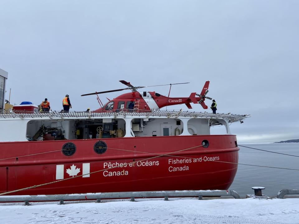 The stern of a Fisheries and Oceans Canada vessel is shown docked with a helicopter and crew on the deck.