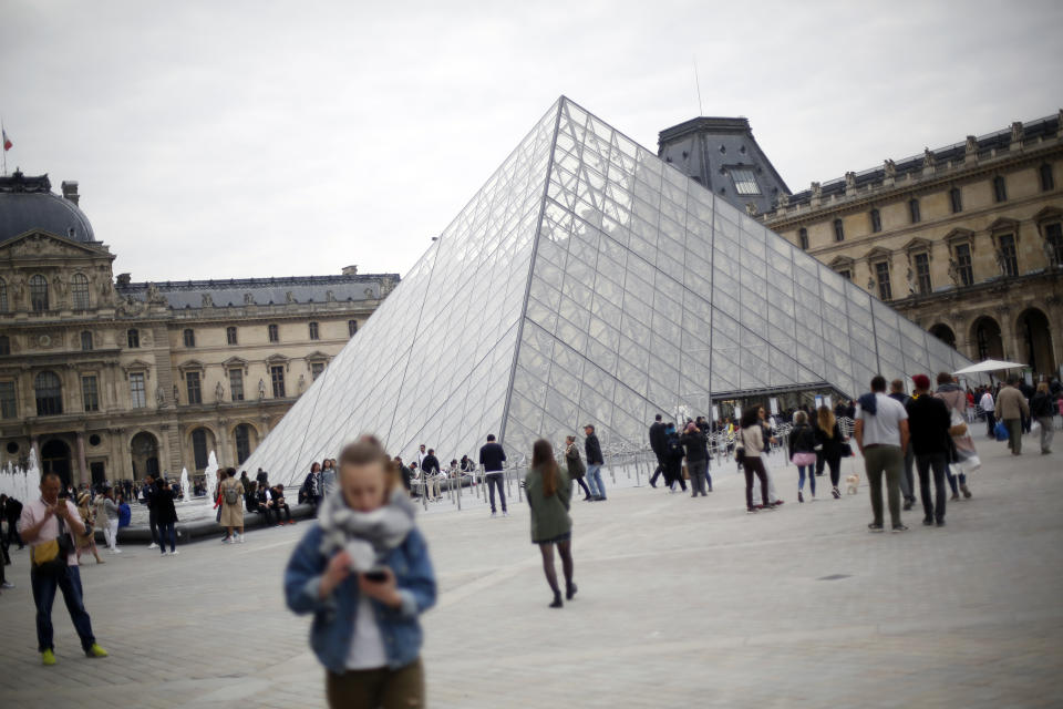 Tourists walk around the pyramide of the Louvre museum, in Paris, Friday, May 17, 2019. Paris' Louvre museum is paying tribute to the architect of its giant glass pyramid, I.M. Pei, who has died at age 102. (AP Photo/Thibault Camus)