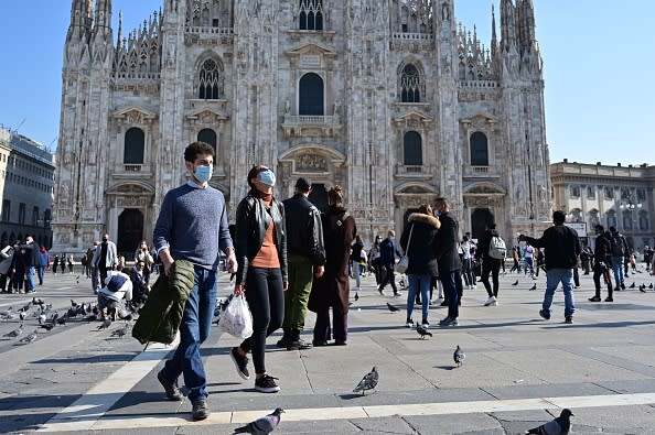 People wearing protective masks walk across the Piazza del Duomo in Milan.