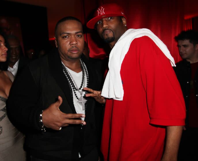 Timbaland wearing black cardigan and white shirt poses with Magoo who is wearing an oversized red t-shirt and red cap