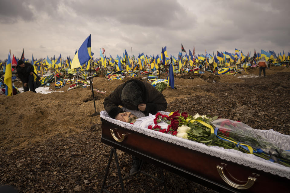 Natalya, the wife of Hennadii Kovshyk, who was killed on the frontline in eastern Ukraine, touches his face before his burial, backdropped by Ukrainian flags placed at the graves of servicemen killed since the war started, in Kharkiv, Ukraine, Thursday, Feb. 16, 2023. (AP Photo/Vadim Ghirda)