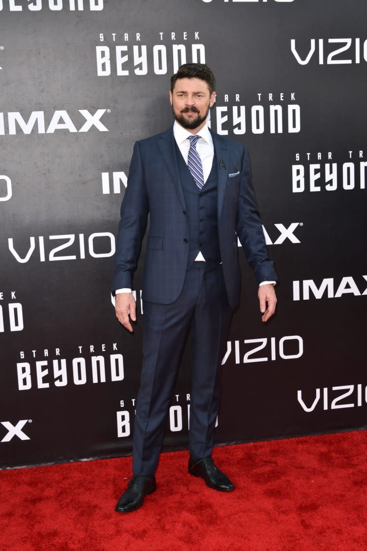 Karl Urban wearing a three-piece navy blue suit. 