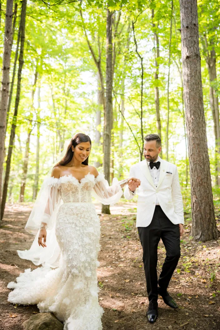 A groom helps his bride walk through a forest.