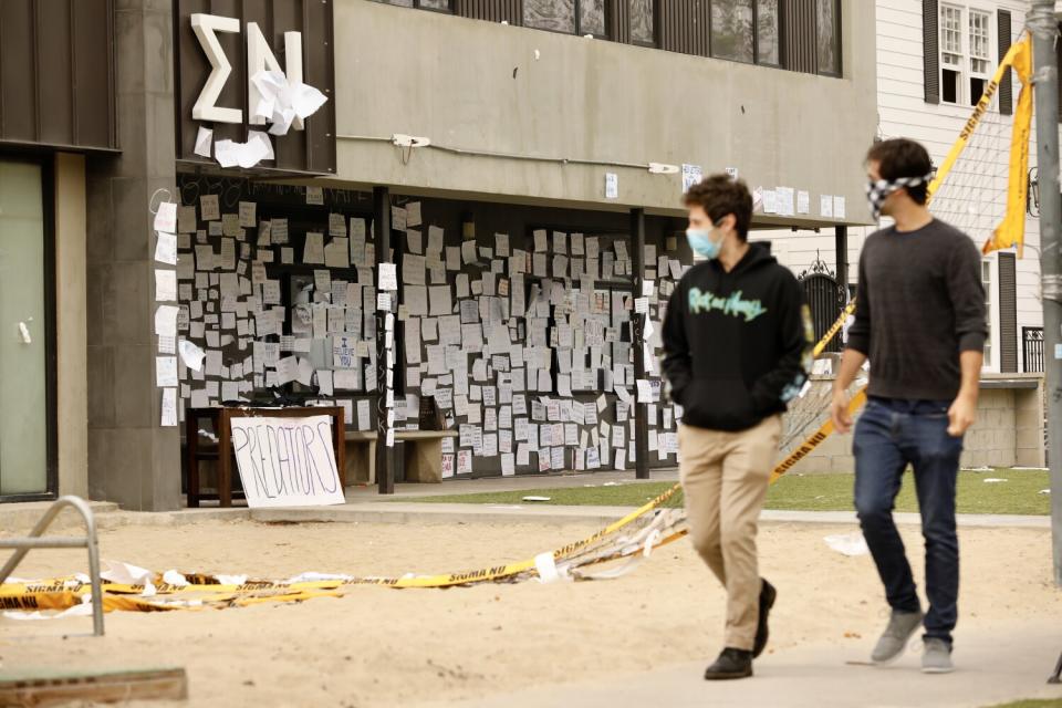 Two male students walk past the Sigma Nu fraternity house, covered in notes