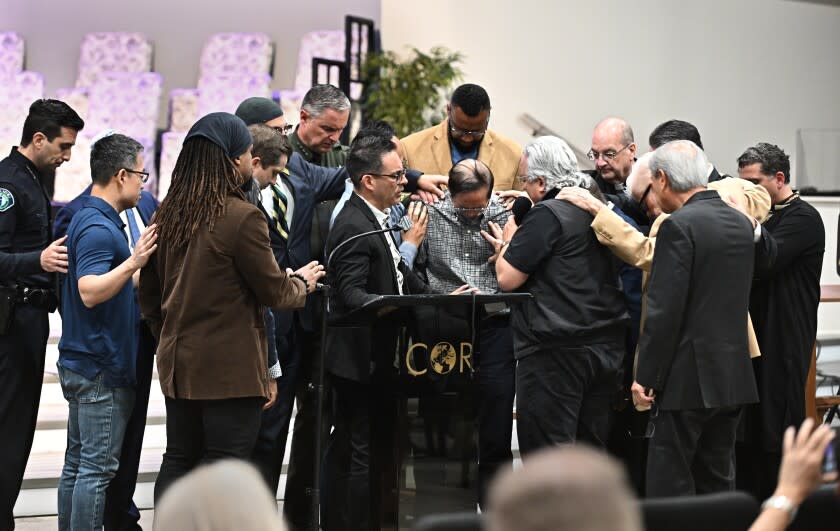 Irvine, California May 16, 2022-Officials pray around former pastor Billy Chang, center, who helped subdue the shooter, tries to hold back his emotions after speaking during a vigil at Christ Our Redeemer Church in Irvine Monday. (Wally Skalij/Los Angeles Times)