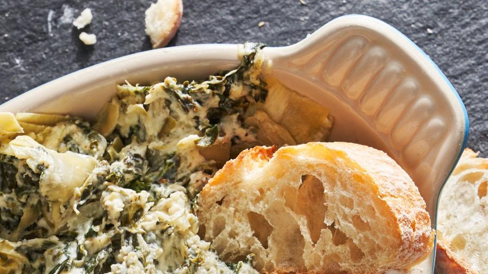 spinach and artichoke dip in a blue dish surrounded by bread slices