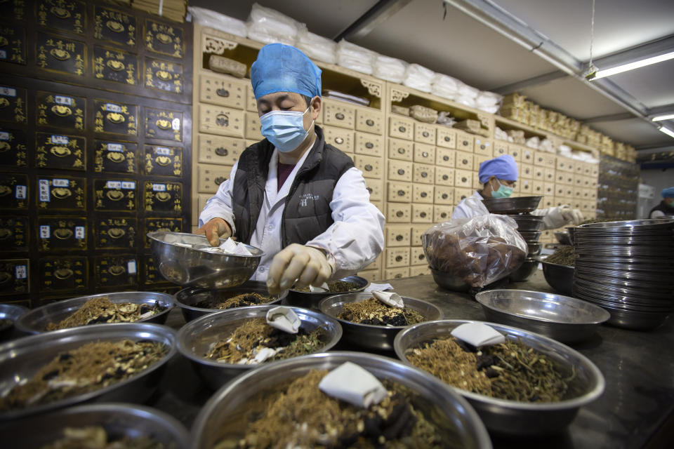 In this March 13, 2020 photo, workers fill orders for prescriptions at the Bo Ai Tang traditional Chinese medicine clinic in Beijing. With no approved drugs for the new coronavirus, some people are turning to alternative medicines, often with governments promoting them. (AP Photo/Mark Schiefelbein)