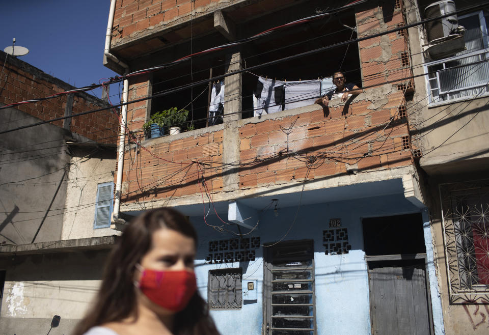 A resident watches from his home's window as water utility workers from CEDAE disinfect the streets in an effort to curb the spread of the new coronavirus in the Mare Complex slum of Rio de Janeiro, Brazil, Monday, May 4, 2020. (AP Photo/Silvia Izquierdo)