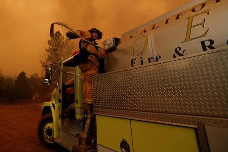 A firefighter pulls a water hose from an engine as he prepares to defend a structure from the Detwiler fire in Mariposa, California U.S. July 19, 2017. REUTERS/Stephen Lam