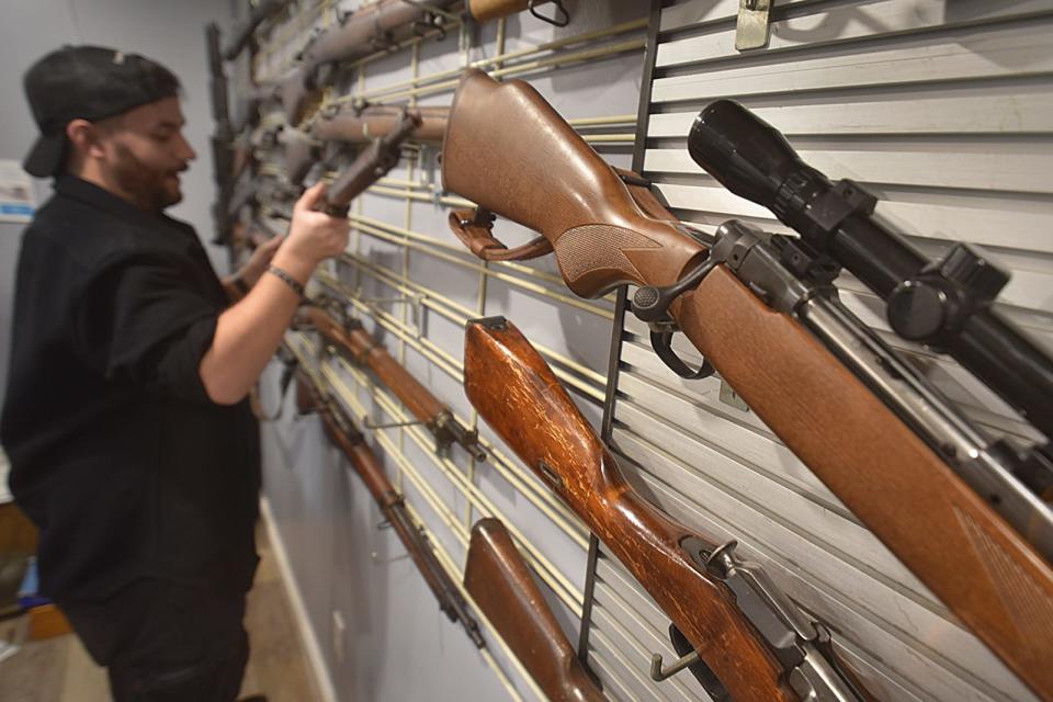 Michael O'Reagan, owner of Collectable Firearms & Militaria on Rhode Island Avenue in Fall River, replaces a rifle on the wall of his shop.