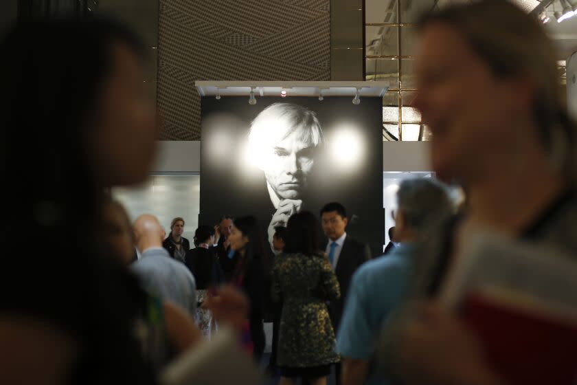 Visitors chat in front of a poster of the late American pop art artist Andy Warhol during the opening ceremony for Christie's first sale in mainland China in Shanghai Tuesday, Sept 24, 2013. (AP Photo)