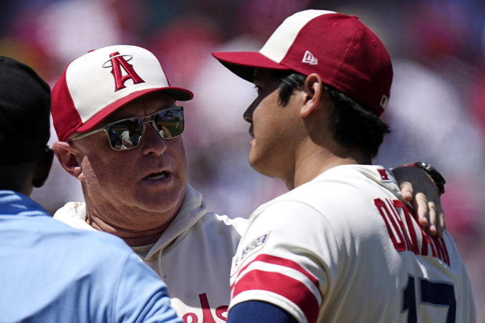 Los Angeles Angels managers Phil Nevin, center, talks with starting pitcher Shohei Ohtani before taking him out of the game due to arm fatigue during the second inning of a baseball game against the Cincinnati Reds Wednesday, Aug. 23, 2023, in Anaheim, Calif. (AP Photo/Mark J. Terrill)