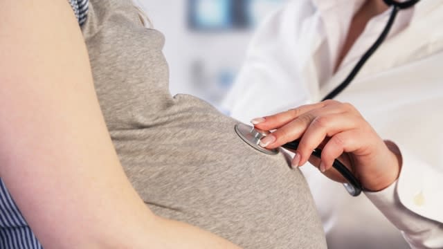 A doctor uses stethoscope on a pregnant person's stomach.