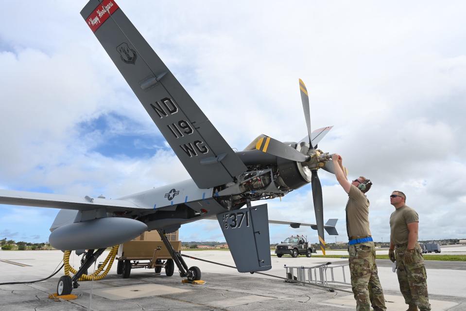 Two men in army uniforms adjust the propellor of a small aircraft.