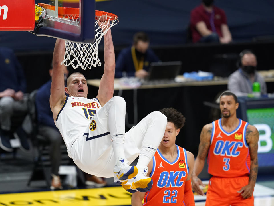 Denver Nuggets center Nikola Jokic, left, hangs from the rim after dunking the ball for a basket against Oklahoma City Thunder forward Isaiah Roby, center, and guard George Hill in the first half of an NBA basketball game Tuesday, Jan. 19, 2021, in Denver. (AP Photo/David Zalubowski)