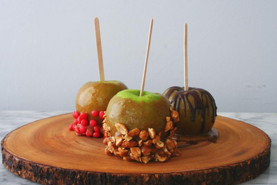 Three vegan caramel apples with an assortment of toppings.