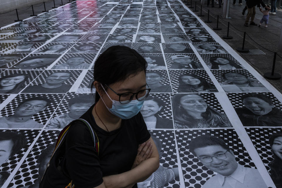 FILE - A pedestrian passes smiling portraits on display as part of the installation titled "Inside Out: Harbour and the City" created by French artist JR in Hong Kong, April 26, 2023. Living in Hong Kong today means juggling contradictory feelings. In 20 interviews, many said that when they focus on business indicators and everyday life, they see a recovery gathering pace after years of travel restrictions. But when it comes to anything political, the openness and freedoms that were once hallmarks of the Chinese-ruled former British colony seem permanently gone. (AP Photo/Louise Delmotte, File)