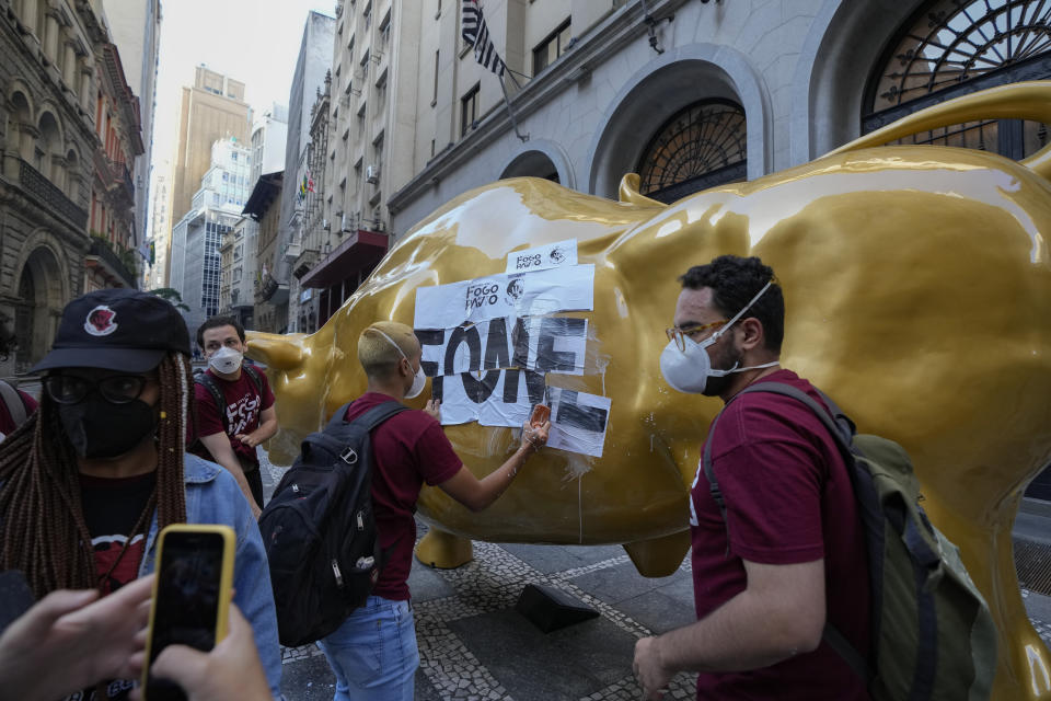 Activists paste the Portuguese word "hungry" on the Golden Bull, a replica of Wall street Charging Bull symbolizing the financial market, outside the Brazilian B3 Stock Exchange in Sao Paulo, Brazil, Wednesday, Nov. 17, 2021. (AP Photo/Andre Penner)