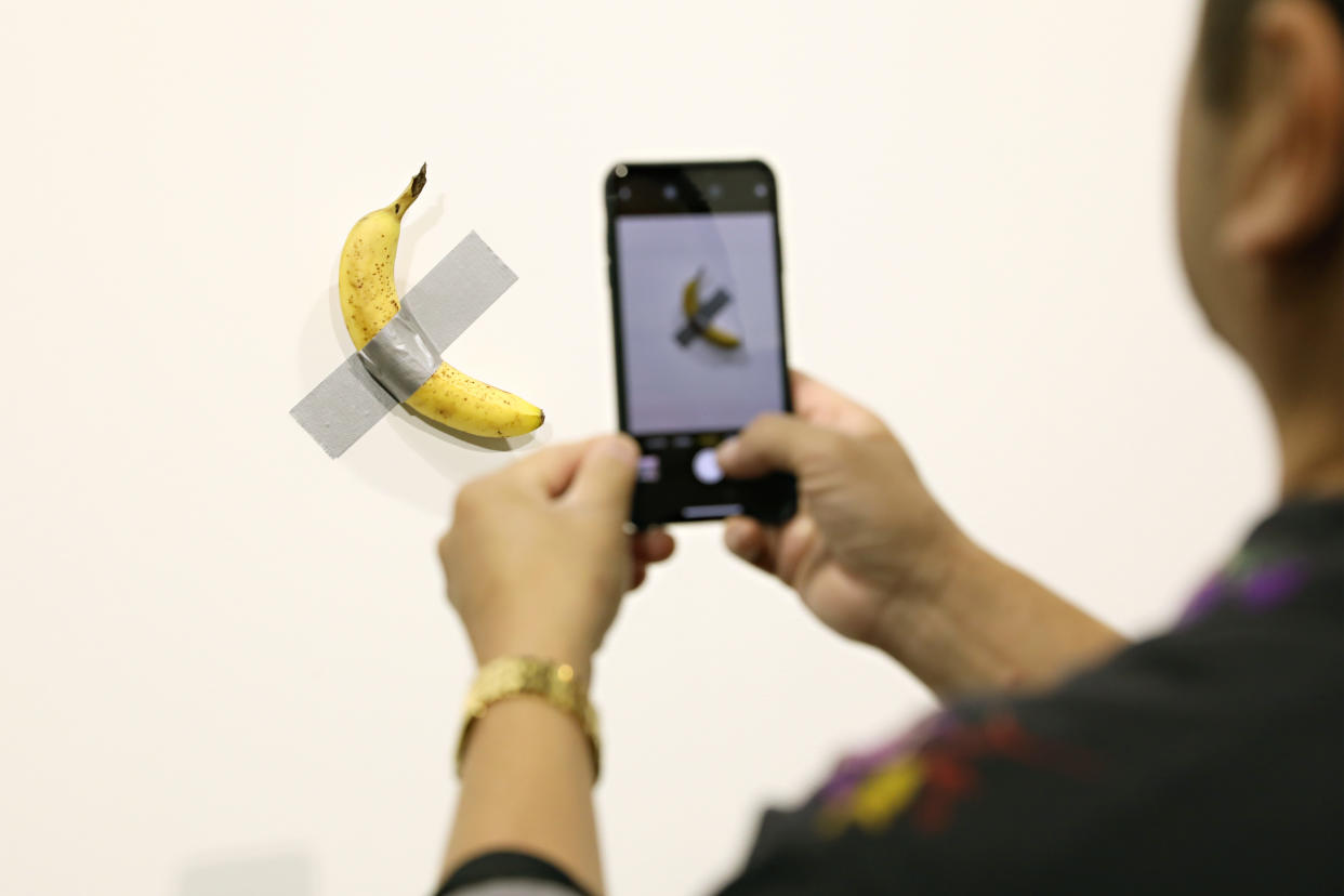 MIAMI BEACH, FL - DECEMBER 06:  People post in front of Maurizio Cattelan's "Comedian" presented by Perrotin Gallery and on view at Art Basel Miami 2019 at Miami Beach Convention Center on December 6, 2019 in Miami Beach, Florida. Two of the three editions of the piece, which feature a banana duct-taped to a wall, have reportedly sold for $120,000.  (Photo by Cindy Ord/Getty Images)