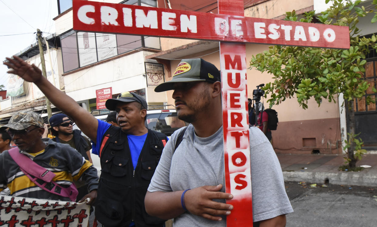 A migrant holds a cross with text that reads in Spanish "State crime. Dead." as he and others start walking north from Tapachula, Chiapas state, Mexico, Sunday, April 23, 2023. Migrants in southern Mexico, angry about 40 of their own who died in a fire at a detention facility last month, began walking toward Mexico City. (AP Photo/Edgar Hernandez Clemente)