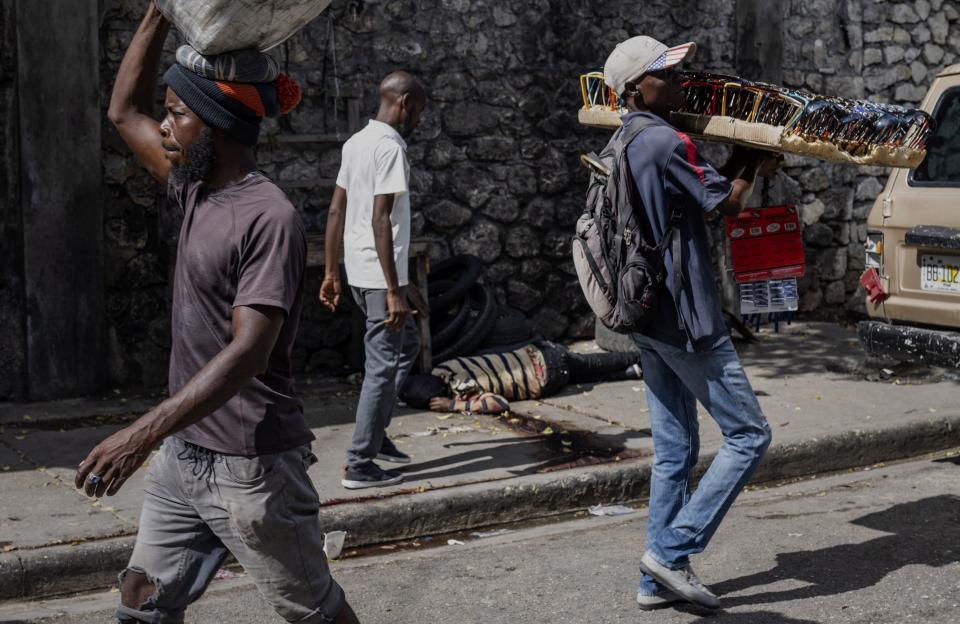 People walk past the bloodied body of a person lying on the sidewalk in Port-au-Prince, Haiti, Wednesday, May 1, 2024. Forensics, who said the body had gunshot wounds, took the body away. (AP Photo/Ramon Espinosa)