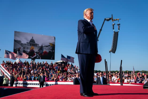 As footage from the Jan. 6, 2021, insurrection at the U.S. Capitol is displayed in the background, former President Donald Trump stands while a song, 