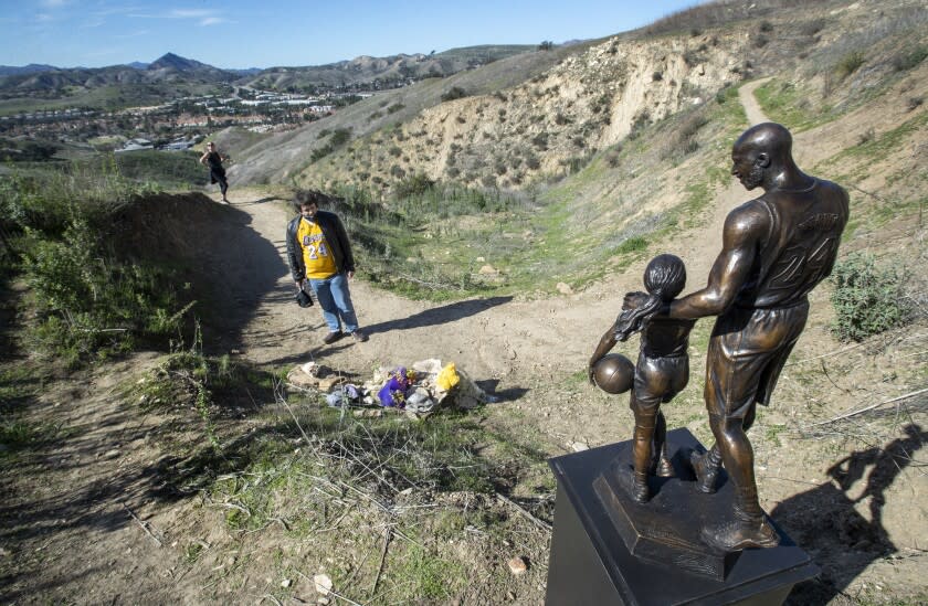 CALABASAS, CA-JANUARY 26, 2022: David Cataldo, 30, of Agoura Hills, visits the crash site in the hills above Las Virgenes Rd in Calabasas that took the lives of Los Angeles Lakers legend Kobe Bryant, his daughter Gianna, and 7 others exactly 2 years ago, on January 26, 2020. In foreground is a bronze statue of Bryant and his daughter Gianna. The statue, weighing about 160 pounds including the steel pedestal, was made by sculptor Dan Medina of West Hills, who had to carry the statue in sections, for the just over 1 mile hike to the crash site. He started out, using a cart and then the cart broke, forcing him to carry it to the crash site. (Mel Melcon / Los Angeles Times)