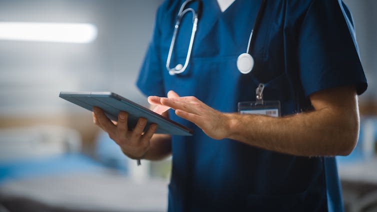 A male doctor wearing scrubs, shown from the neck down.