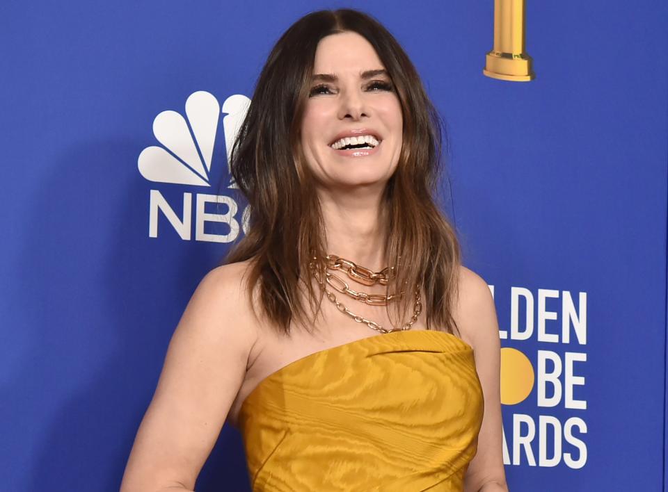 Sandra smiles while wearing a strapless golden colored dress