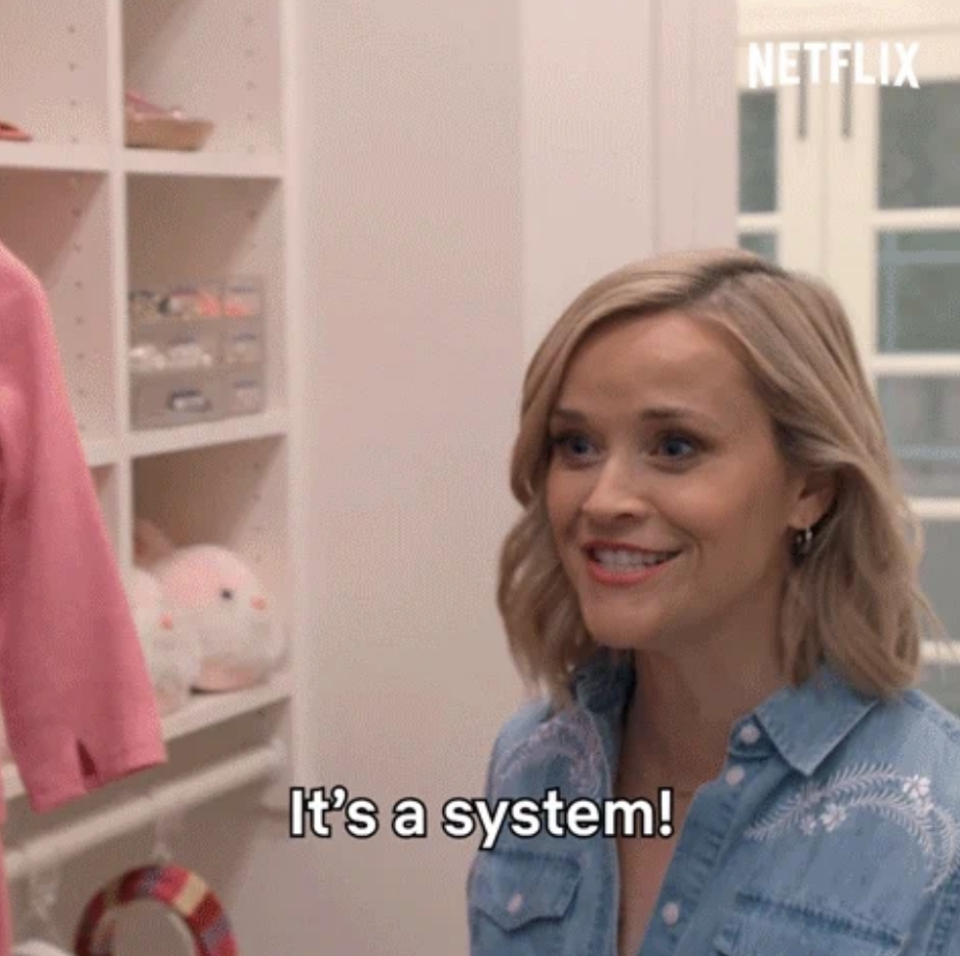 Reese Witherspoon smiles and speaks the caption, "It's a system!", in a home storage area.
