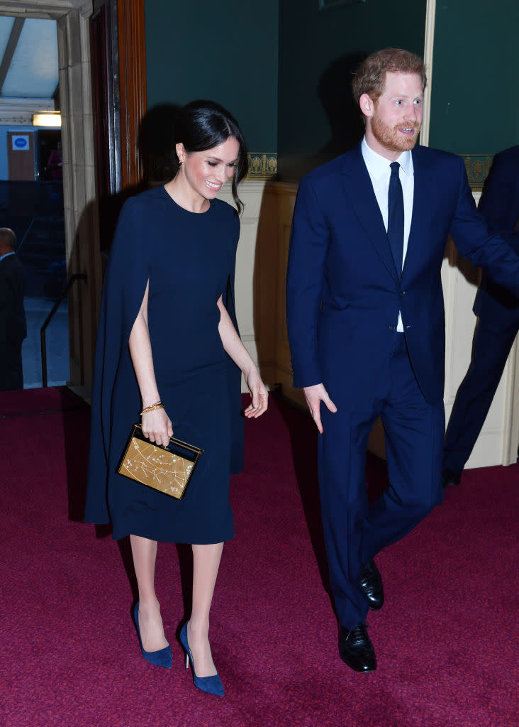 <p>To celebrate the Queen’s 92nd birthday, Prince Harry and Meghan Markle colour co-ordinated for the first time. The former actress donned a navy-hued cape dress by Stella McCartney (with a £1,150 price tag) as she joined the royal family at the Royal Albert Hall. She accessorised the look with a Naeem Khan Armory Zodiac clutch. <em>[Photo: Getty]</em> </p>